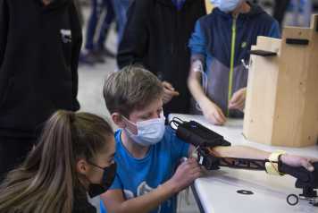Enlarged view: A boy working on a robotic arm with a student helping him