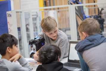 Enlarged view: Children with a robotic arm looking at a laptop to program it